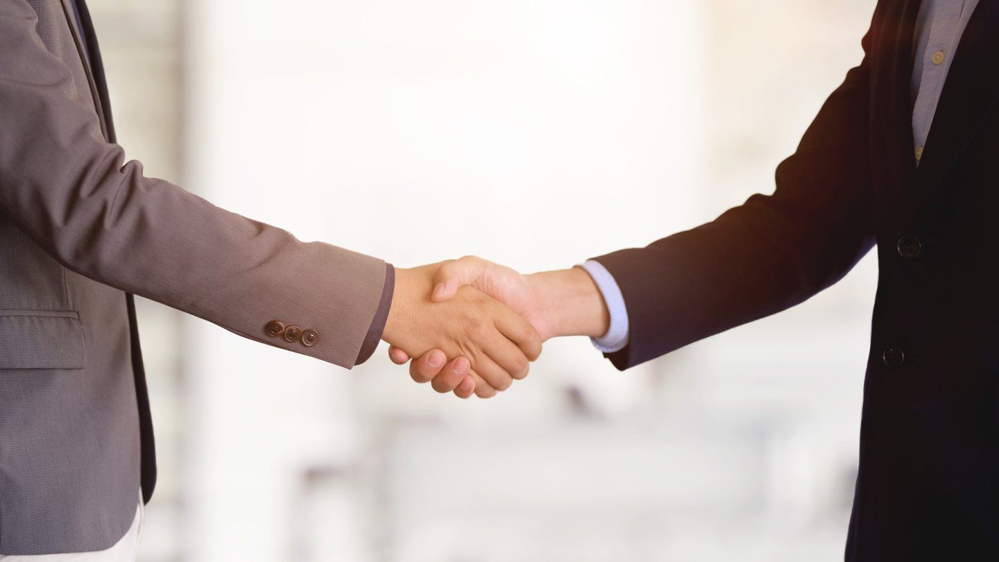 Crop businessmen shaking hands in light office